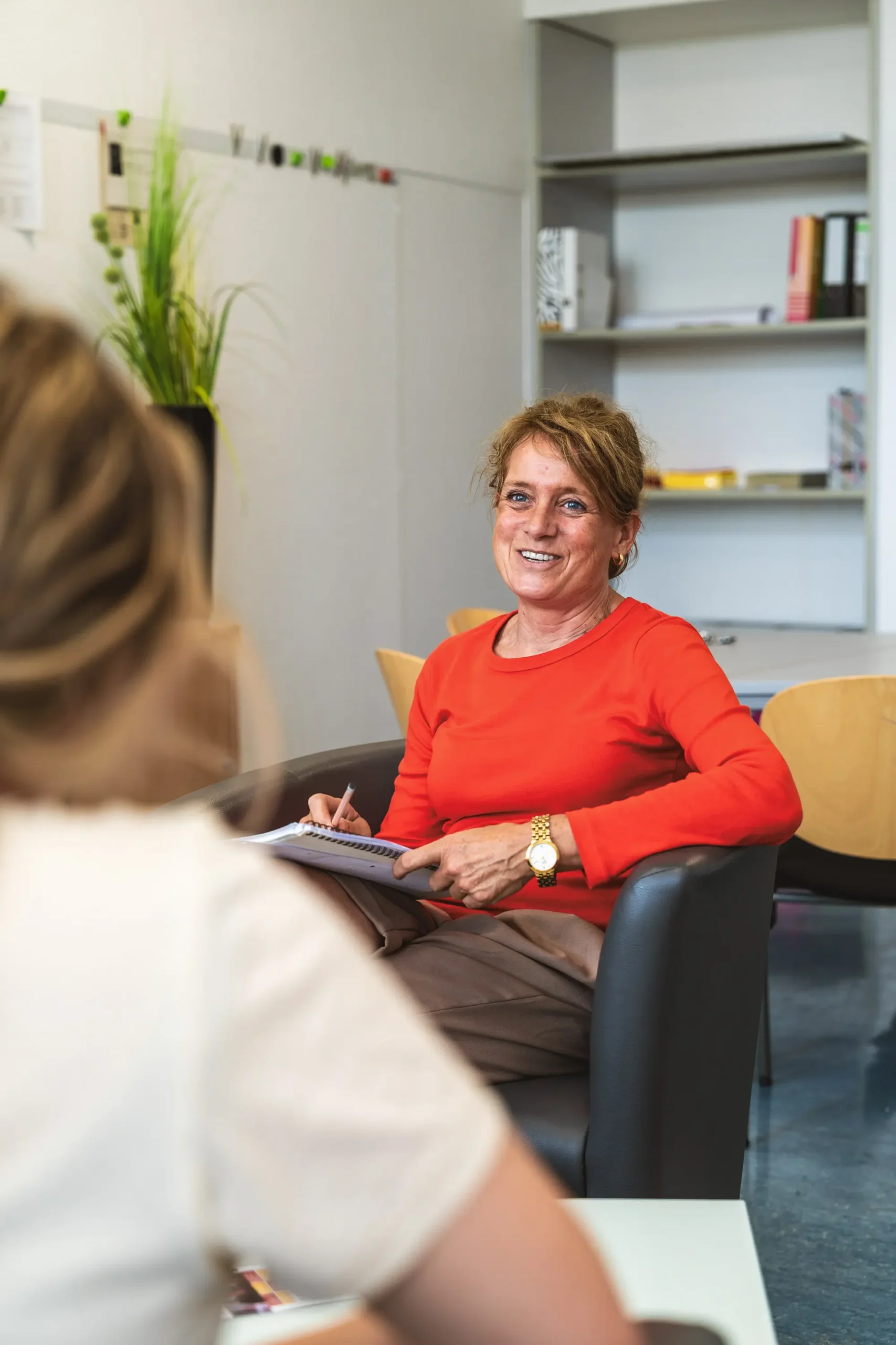 Lächelnde Beraterin im roten Pullover während eines Beratungsgesprächs im Büro.